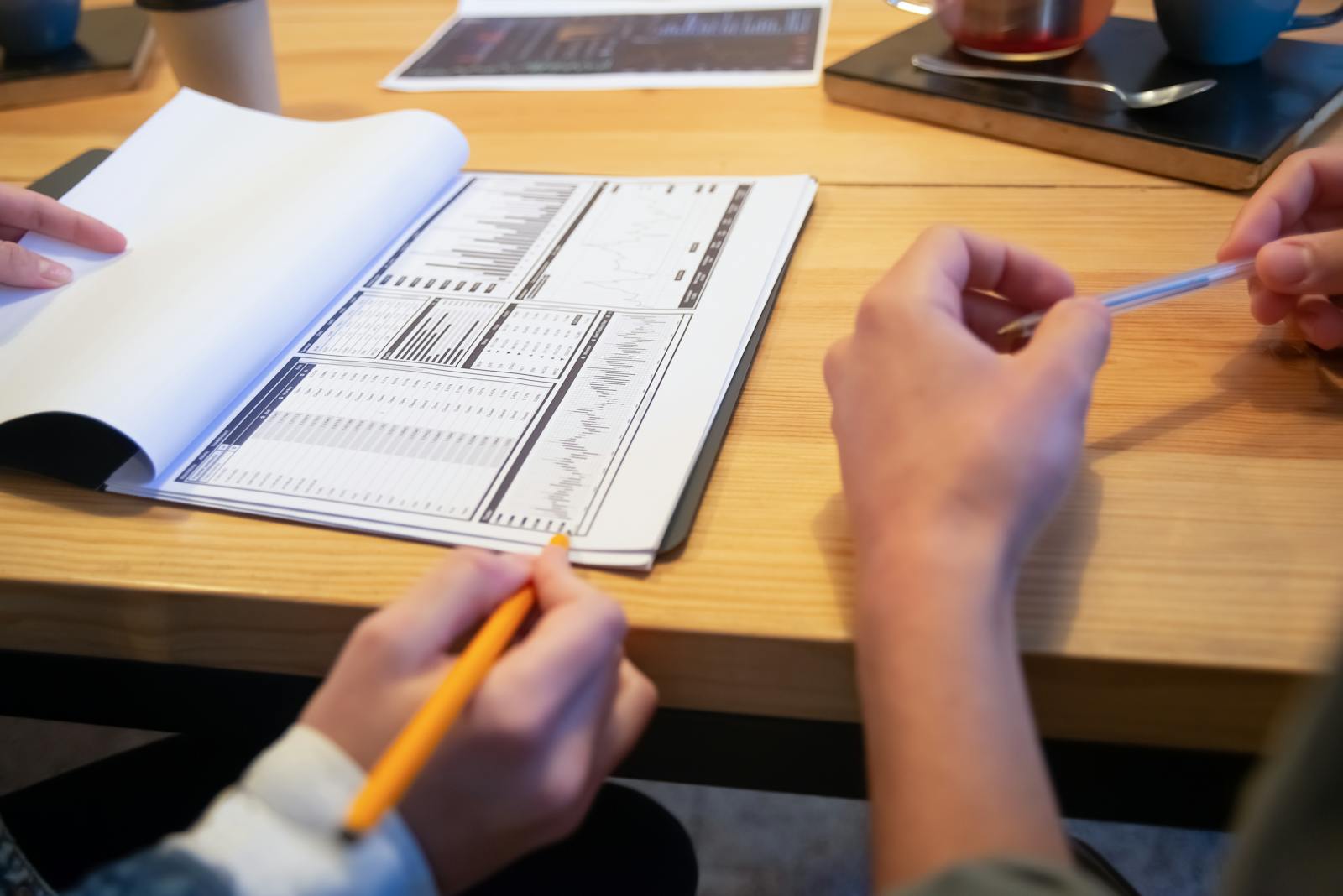 Two pairs of hands reviewing a printed analytics report at a wooden table with coffee