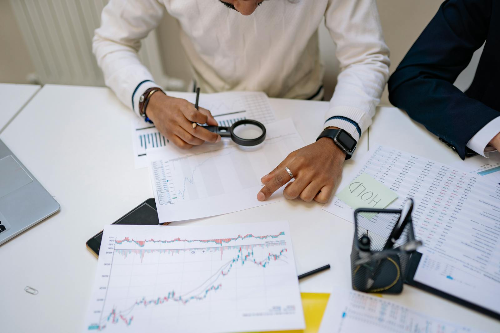 Two professionals at a meeting table reviewing printed charts with a magnifying glass